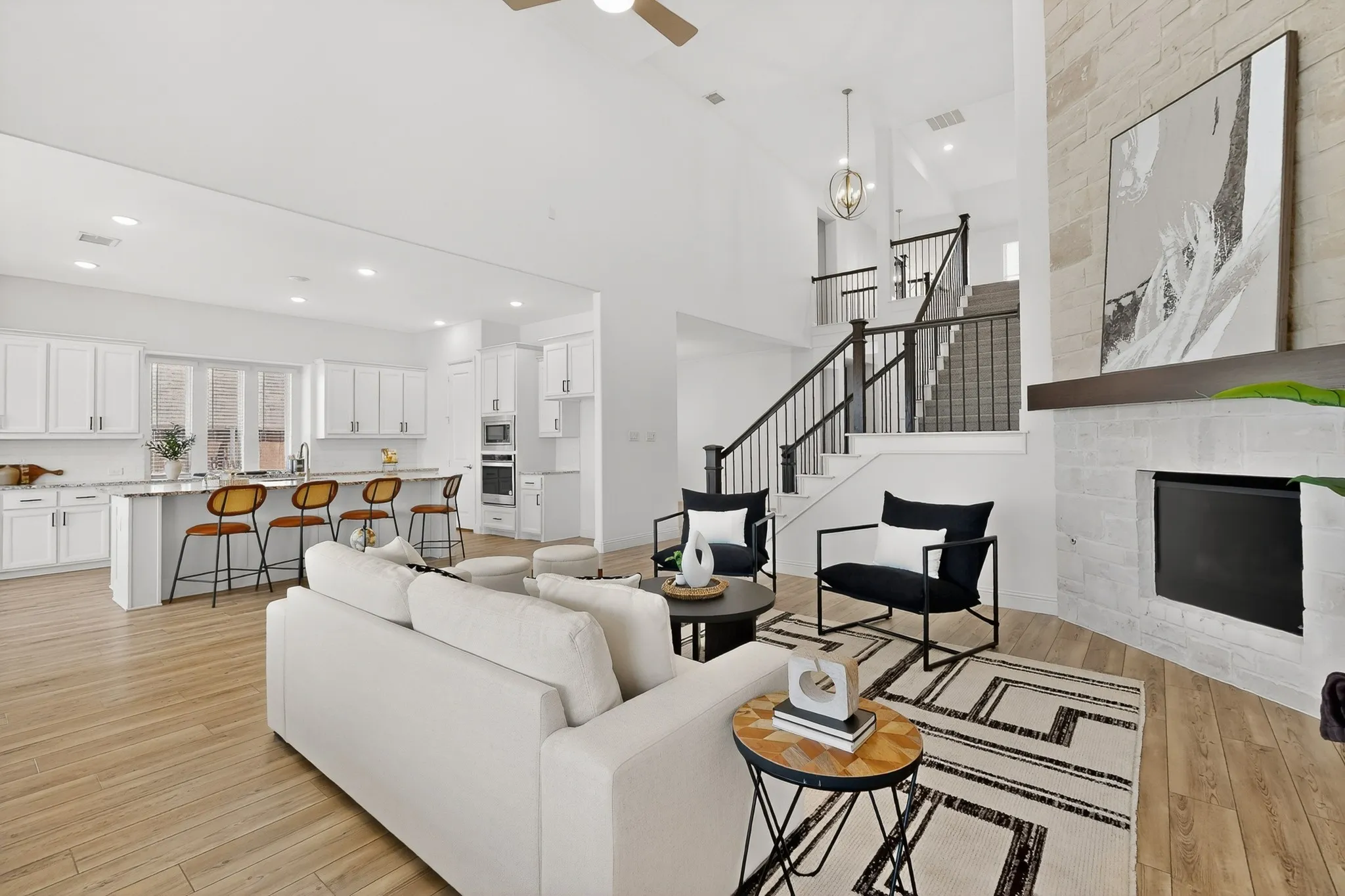 Two-story living area with wood-finish flooring, a stone fireplace, and an open staircase with dark balusters