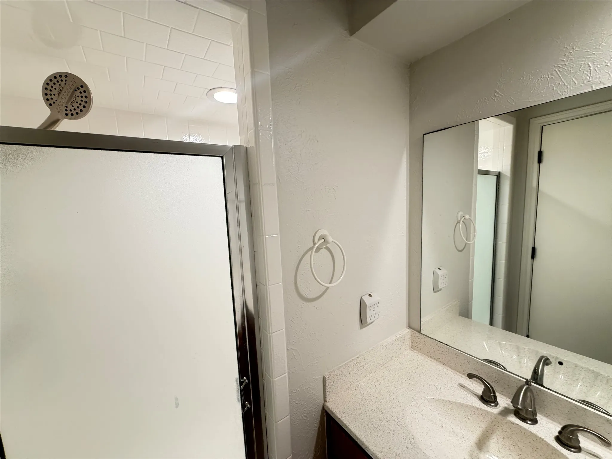 Vanity with a speckled countertop and dual-handle faucet, frameless mirror, and shower with a frosted glass enclosure and a multi-function showerhead