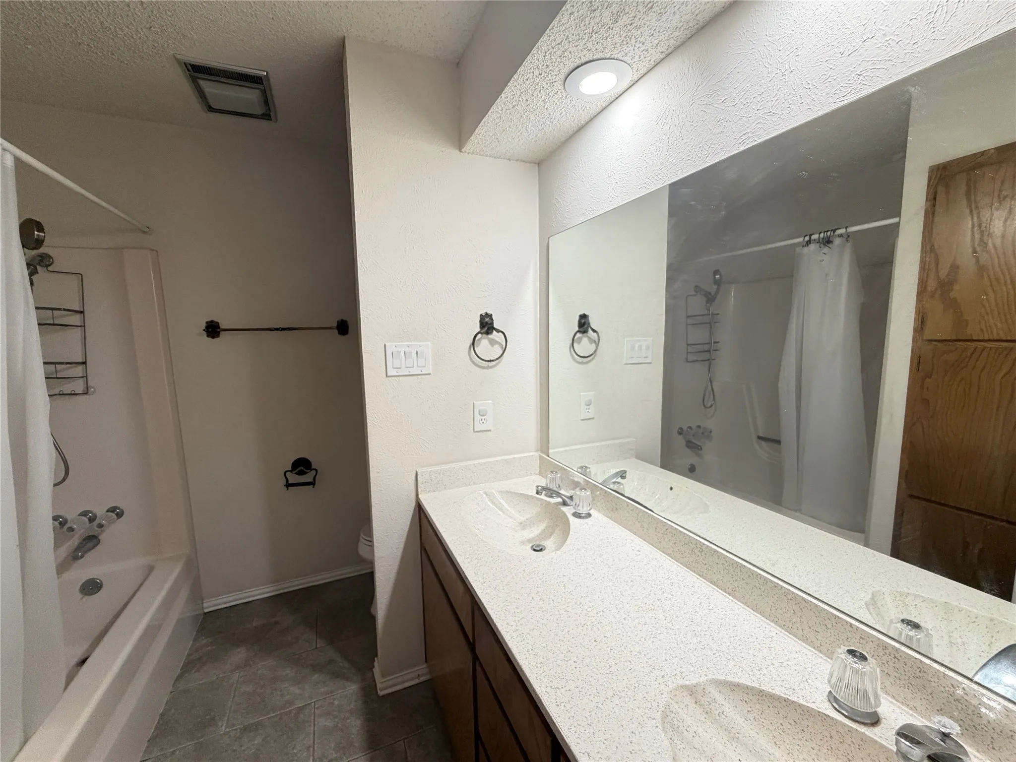 Dual vanity with an integrated countertop, large wall-mounted mirror, and wood-finish cabinetry