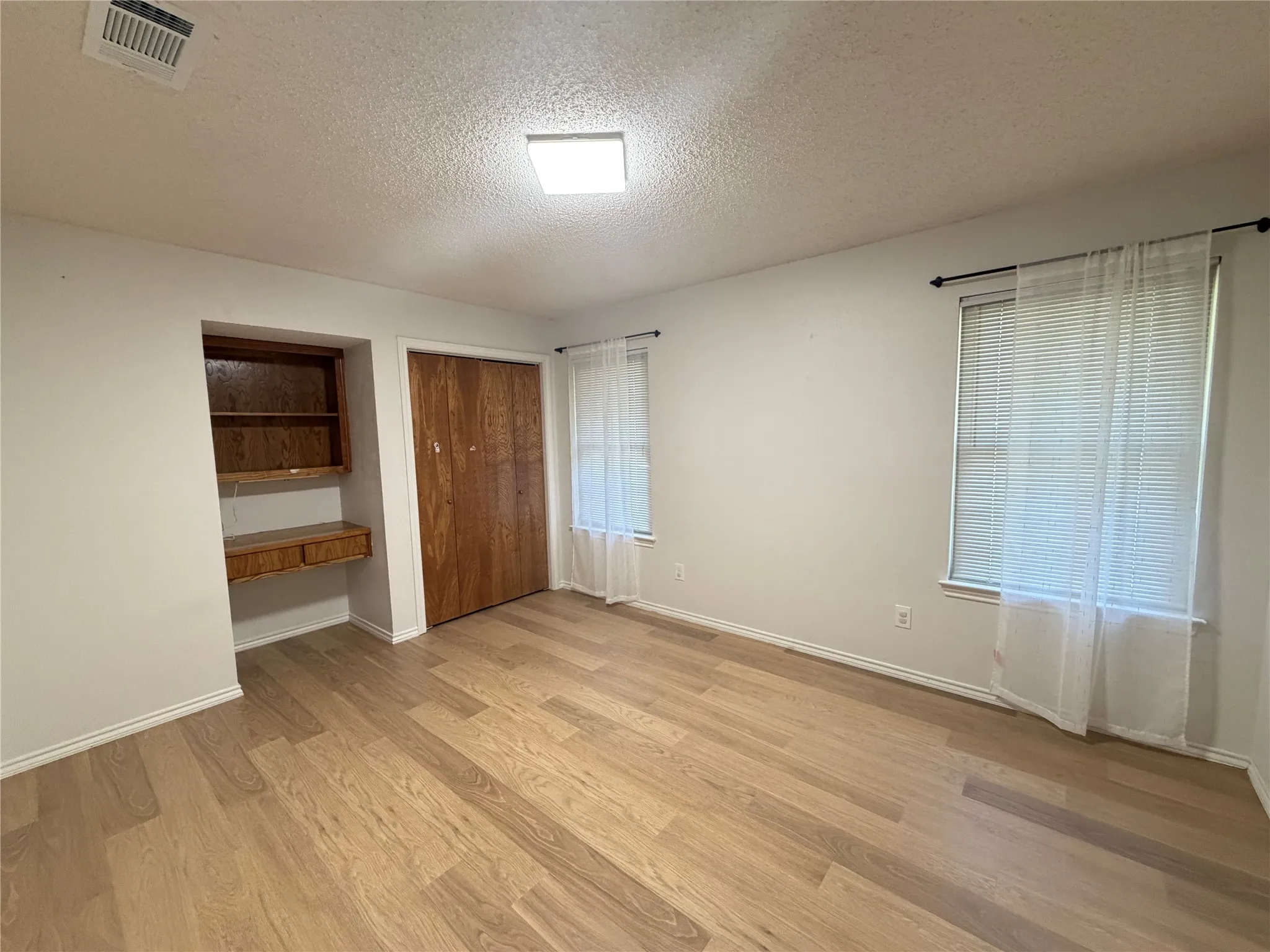 Wood-finish flooring, built-in desk with shelving, recessed lighting, double-door closet, and window with blinds
