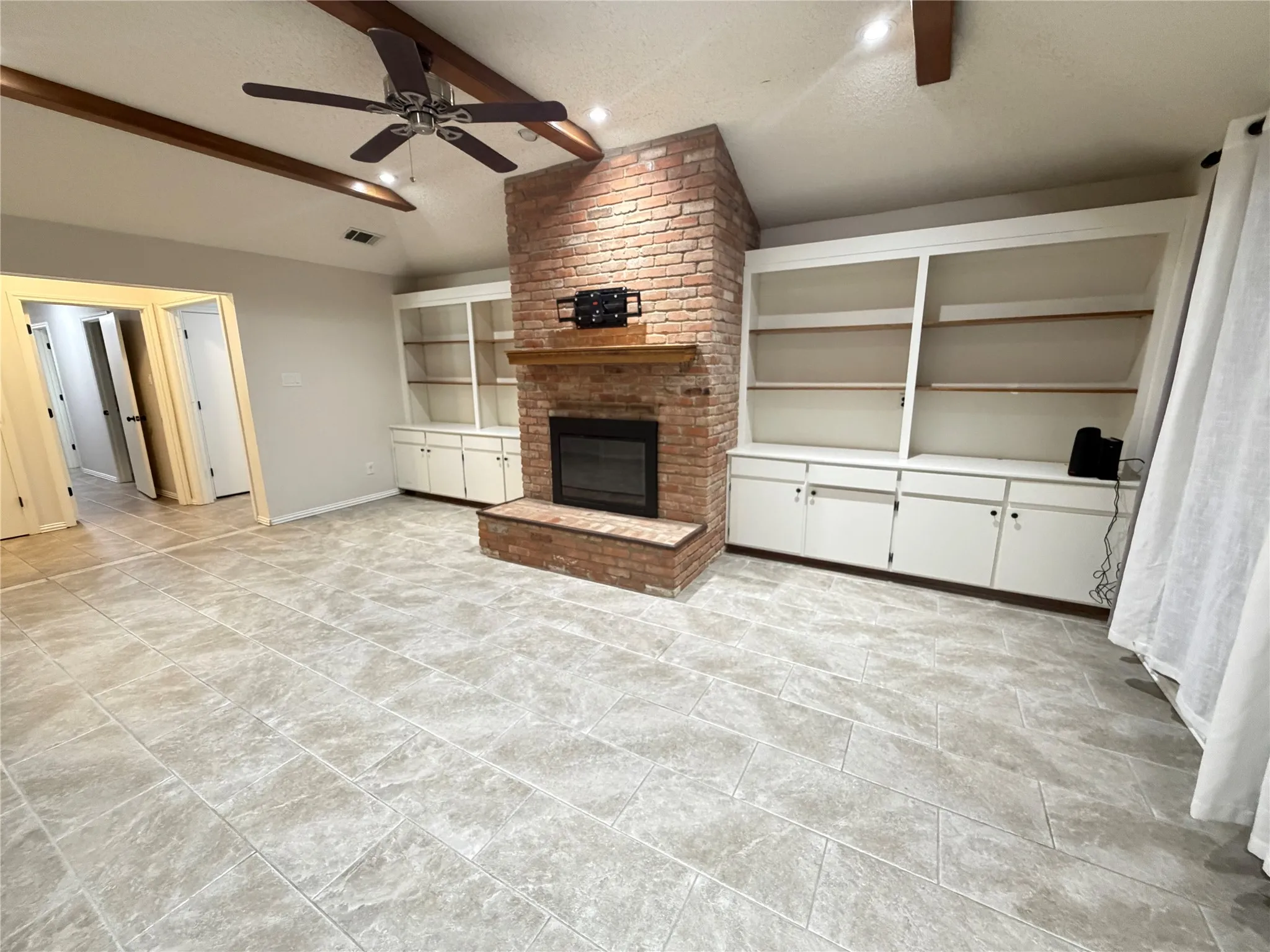 Light-toned tile flooring throughout, brick fireplace with a wood mantle, built-in shelving and cabinetry, and a ceiling fan with integrated lighting