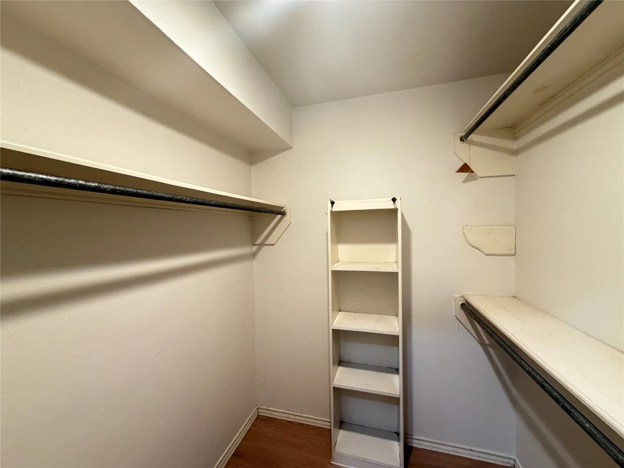 Walk-in closet featuring multiple shelves, hanging rods, and wood-finish flooring
