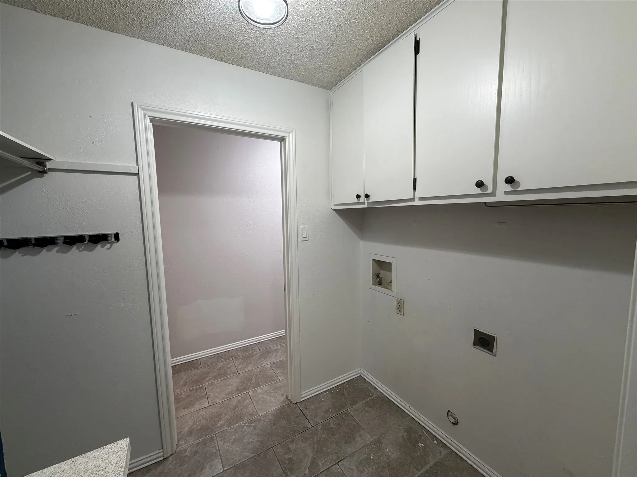 White overhead cabinetry with black hardware, recessed ceiling lighting, tile flooring, and a wall-mounted coat rack