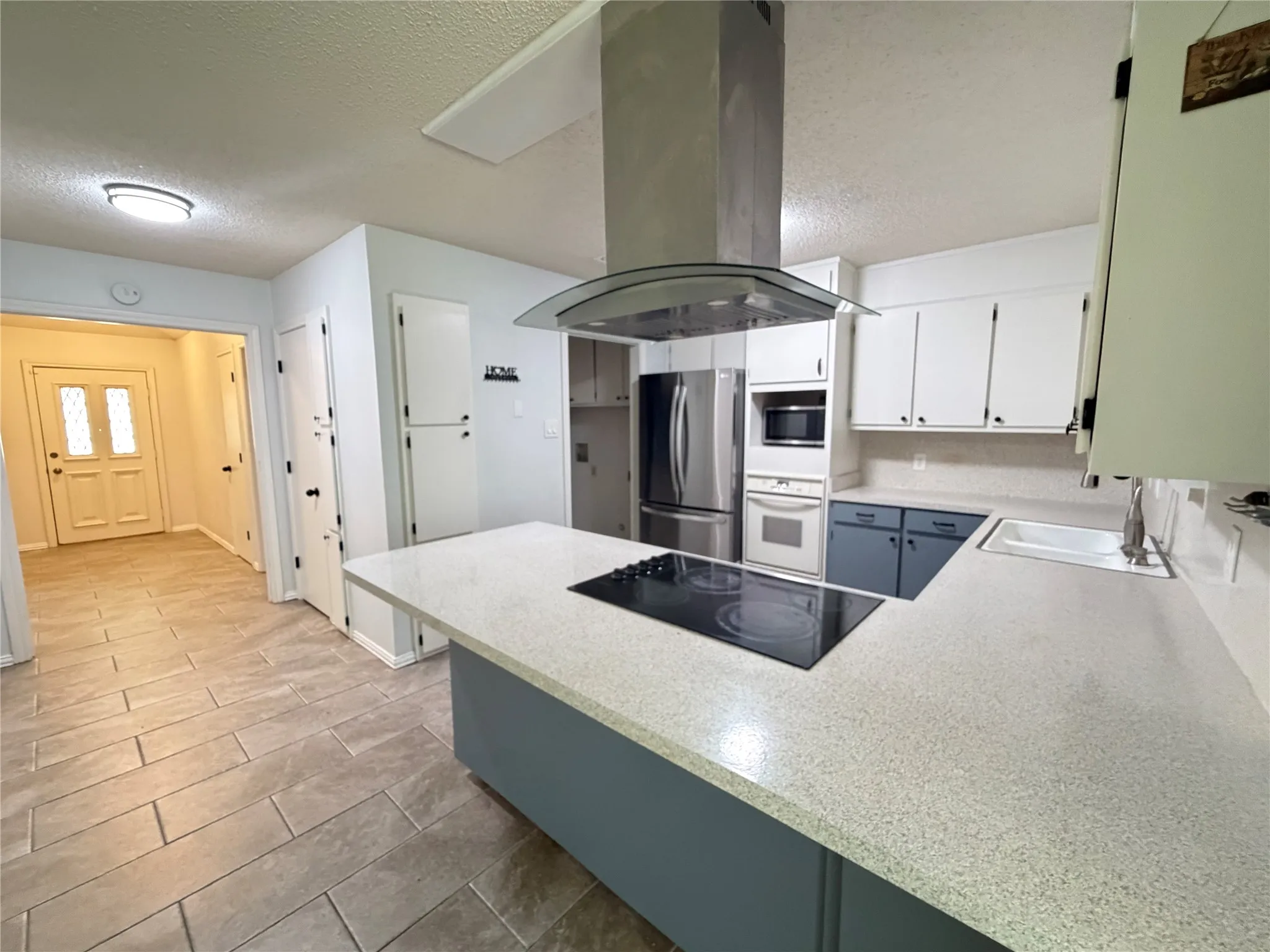 Kitchen featuring a built-in electric cooktop on an island, stainless steel appliances, a range hood, and tile flooring