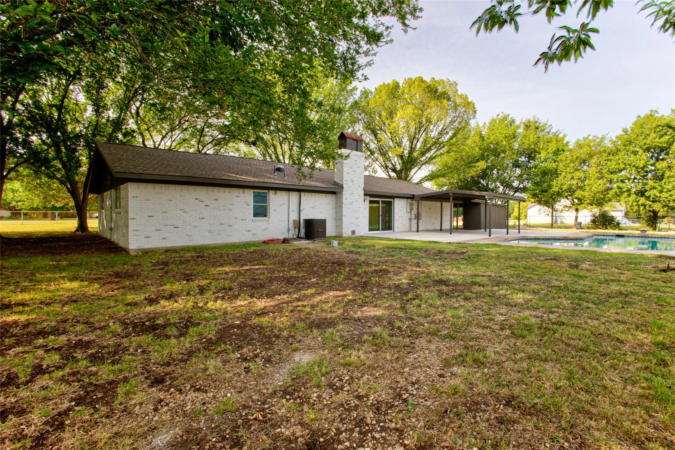 White brick exterior with a dark-shingled roof, a chimney, and a covered patio area