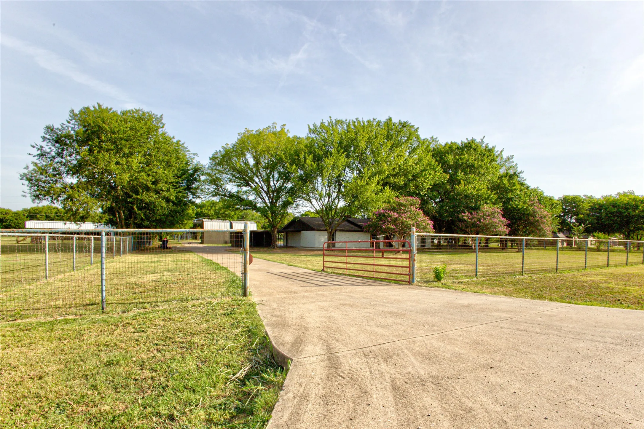 Wide View From The Road Through Pipe Framed Fence & Gated Entry Up The Full Concrete Driveway.