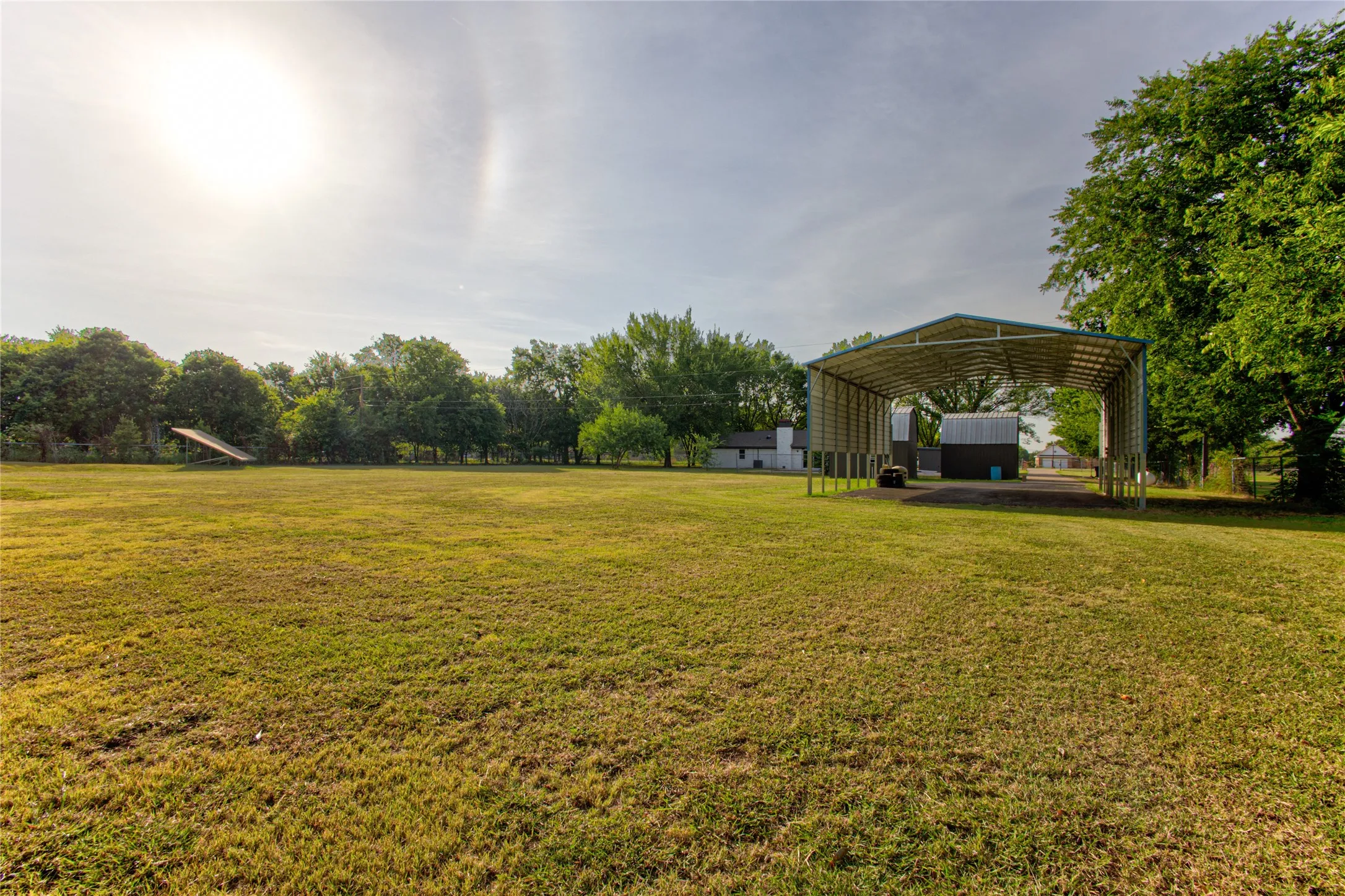 Expansive green space featuring a large metal carport structure and additional outbuilding
