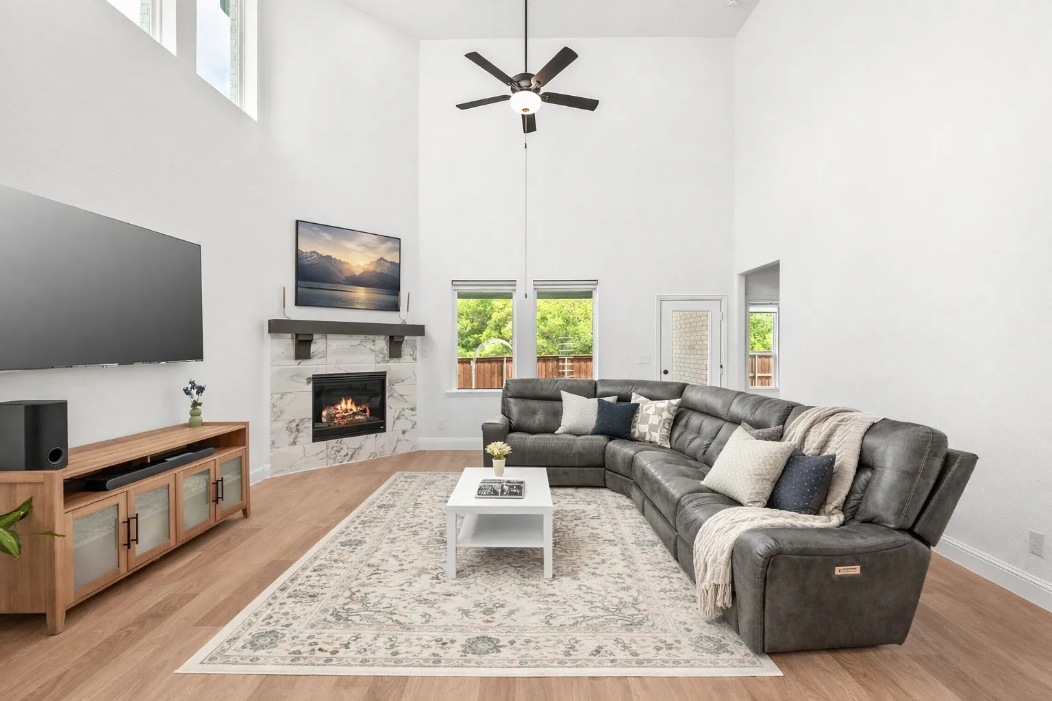 Living room with light wood finished floors, a high end fireplace, a high ceiling, and ceiling fan