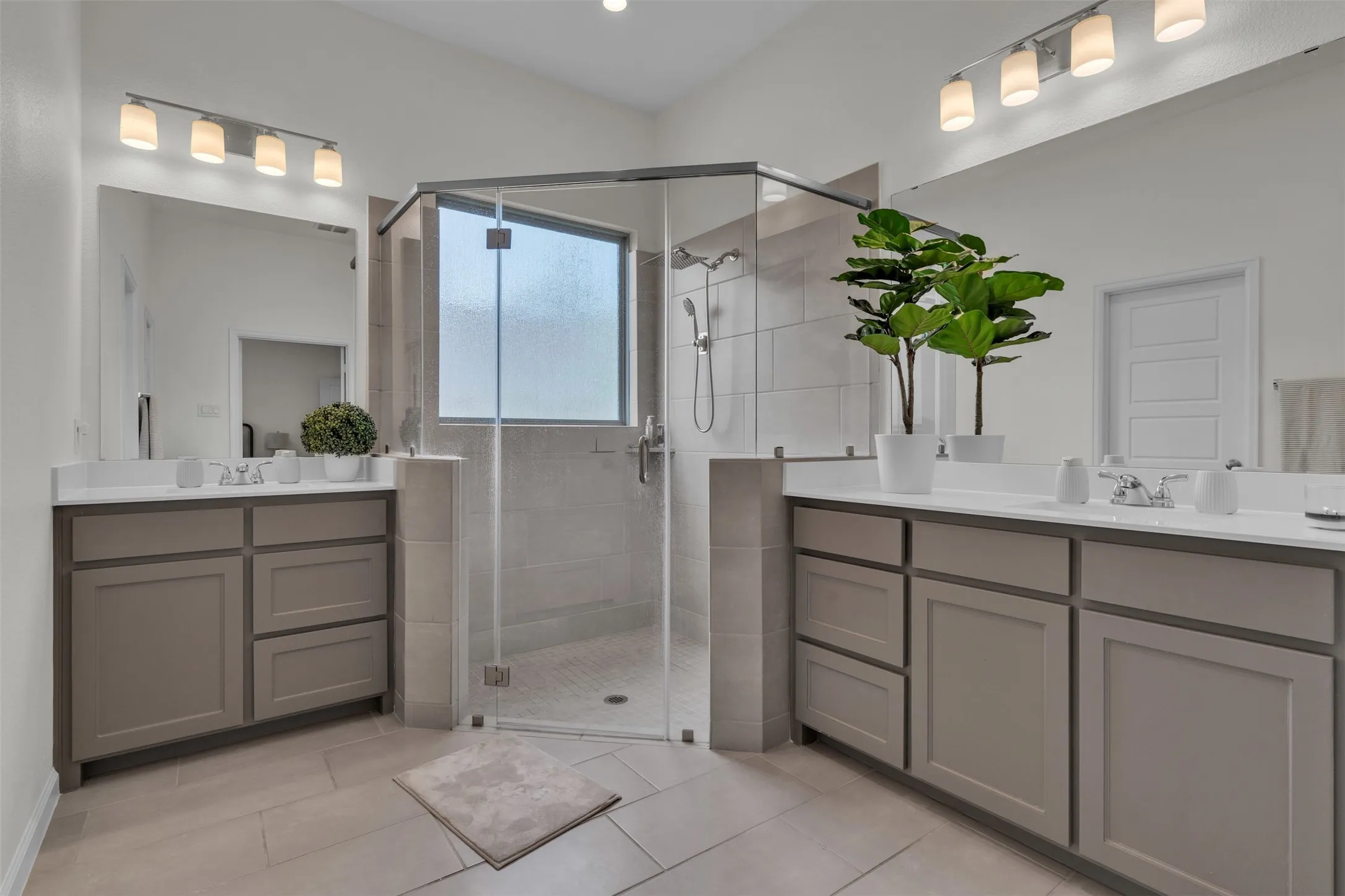 Dual vanities with undermount sinks, quartz countertops, tile flooring, glass-enclosed shower, and a privacy window