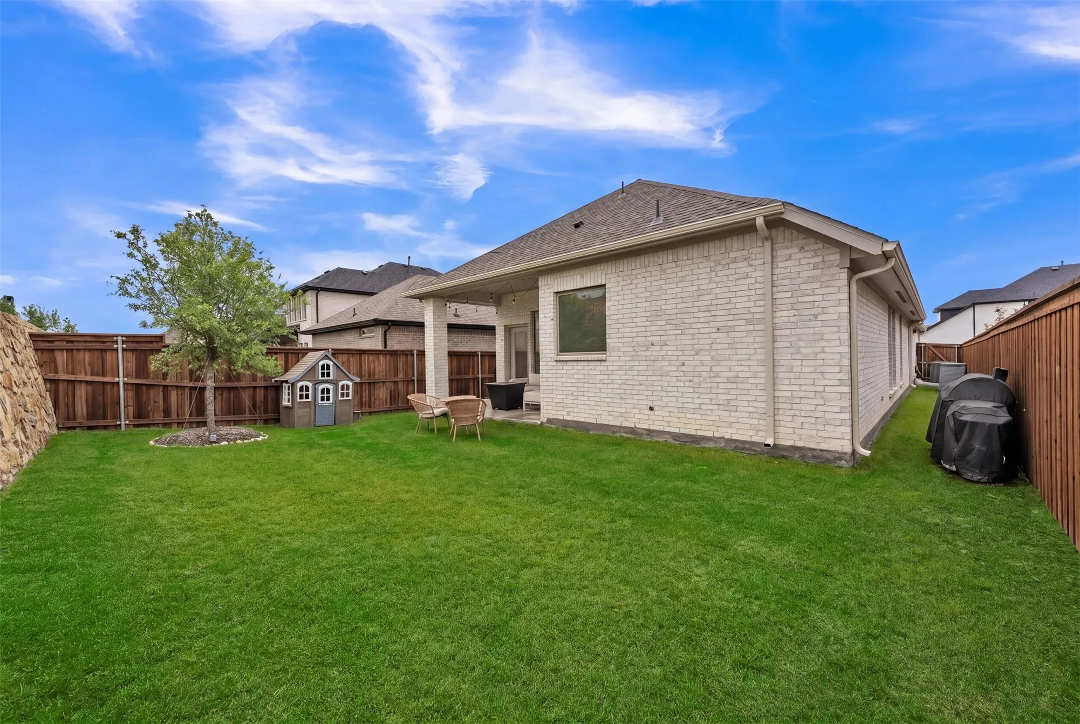 Expansive backyard featuring a manicured lawn, wood fencing, and a stone retaining wall