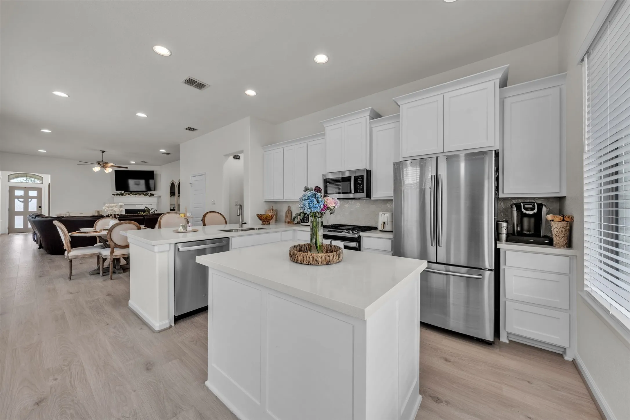 Kitchen featuring a white shaker cabinetry, stainless steel appliances, a center island with a light-toned countertop, and wood-finish flooring