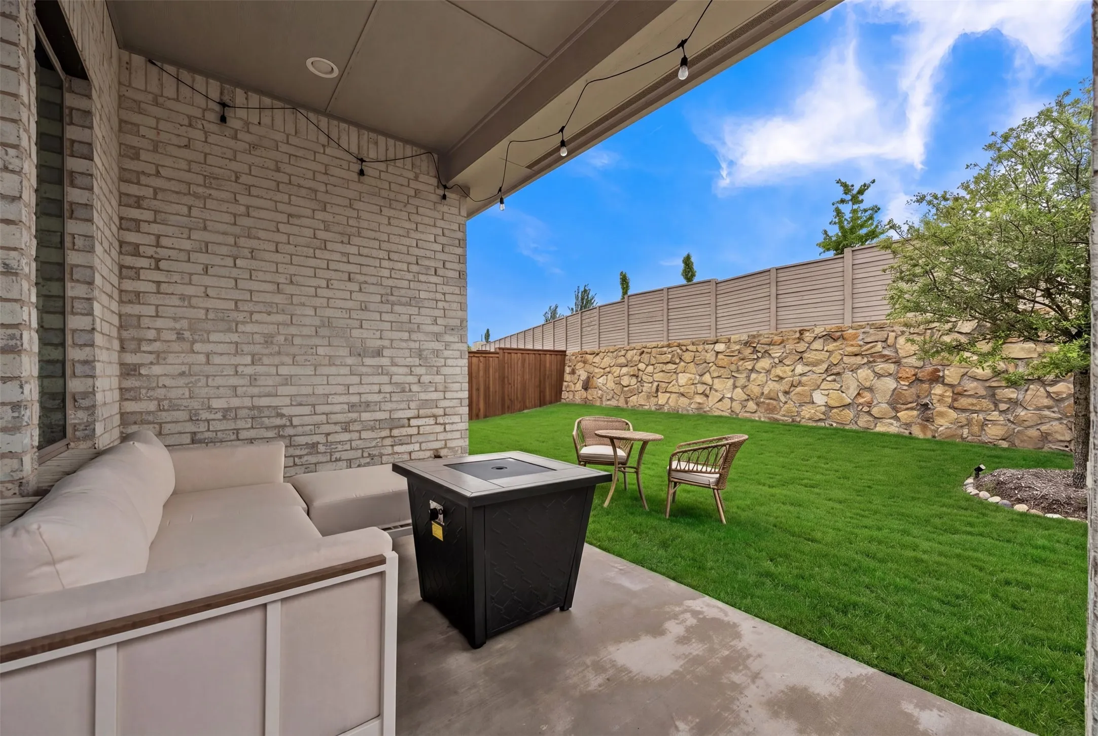 Covered patio with string lighting, concrete flooring, and brick exterior