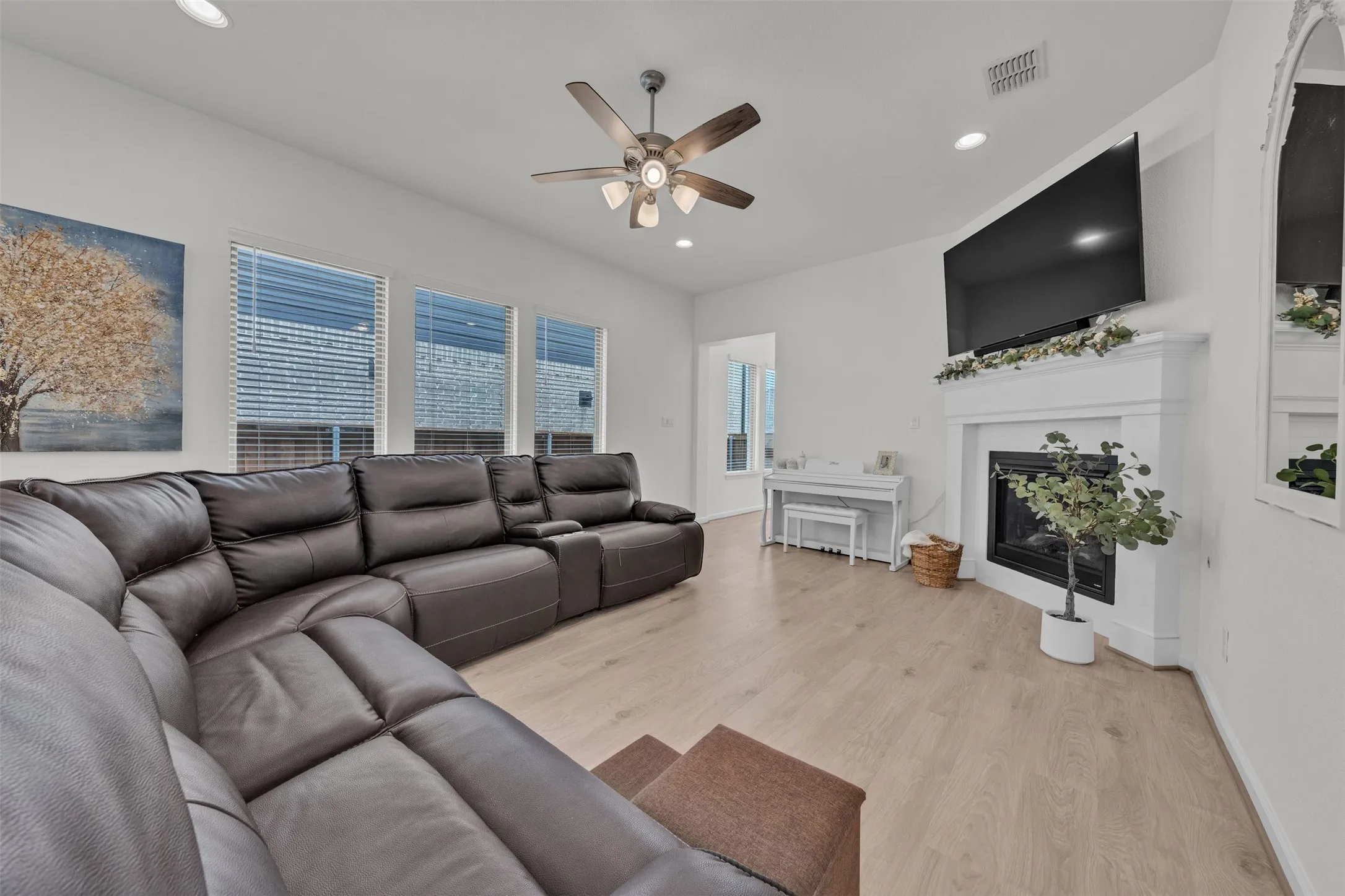 Spacious living area featuring wood-finish flooring, a ceiling fan, recessed lighting, a built-in fireplace with a white mantel, and multiple windows
