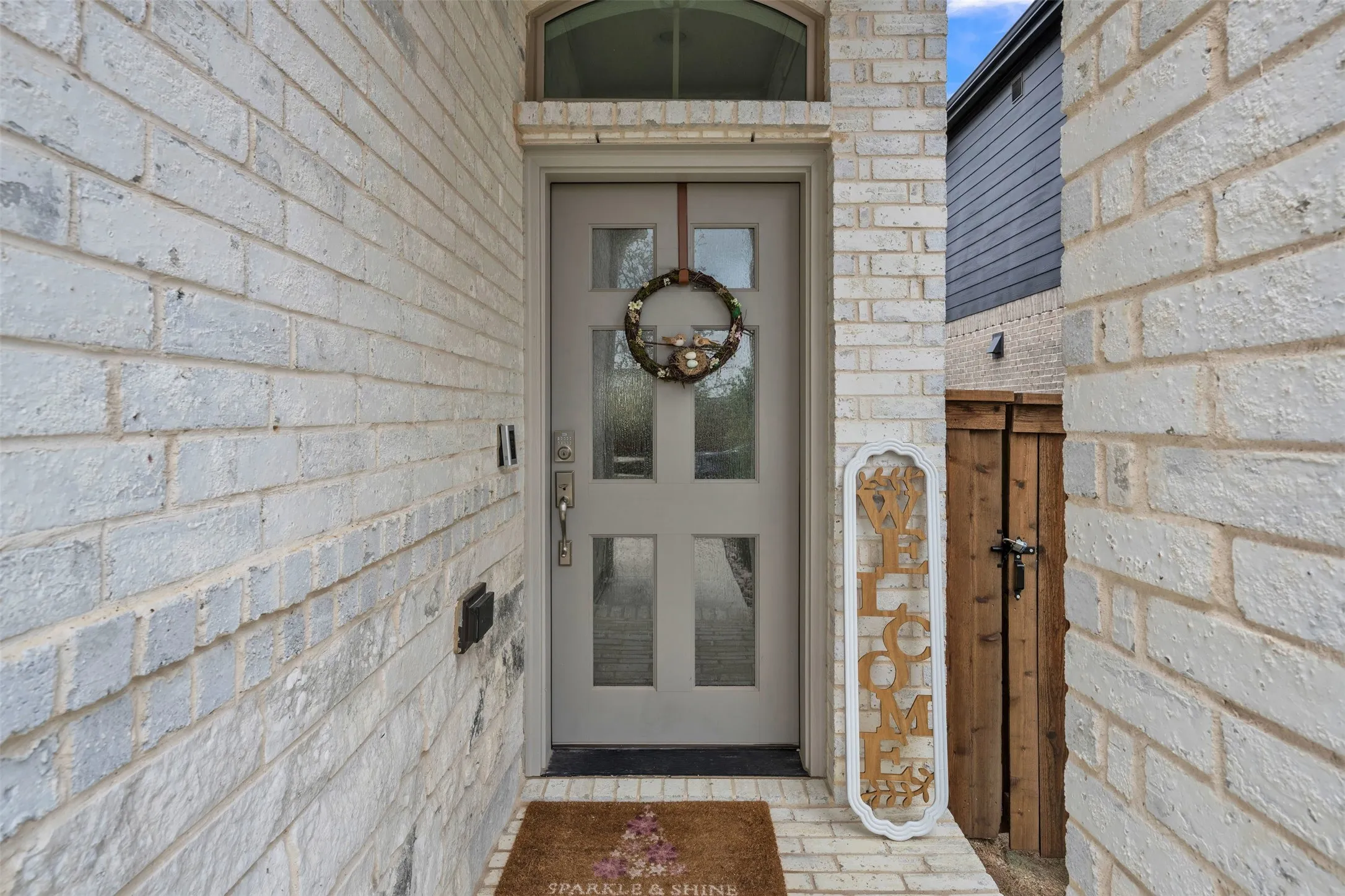 Painted brick exterior with a paneled entry door, transom window, and secured side gate