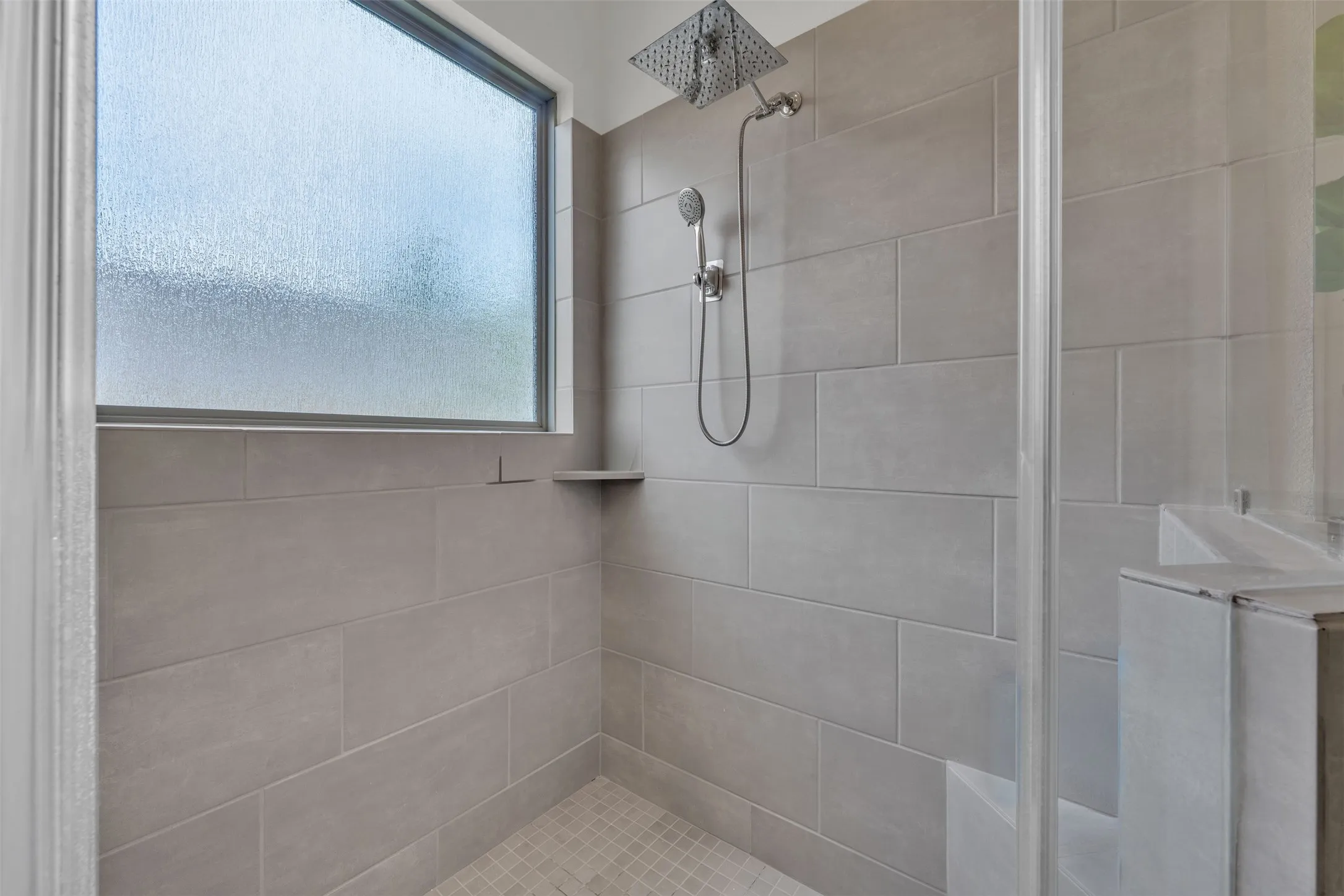 Shower enclosure with large format wall tiling, a rainfall showerhead, a handheld shower fixture, and a built-in frosted window