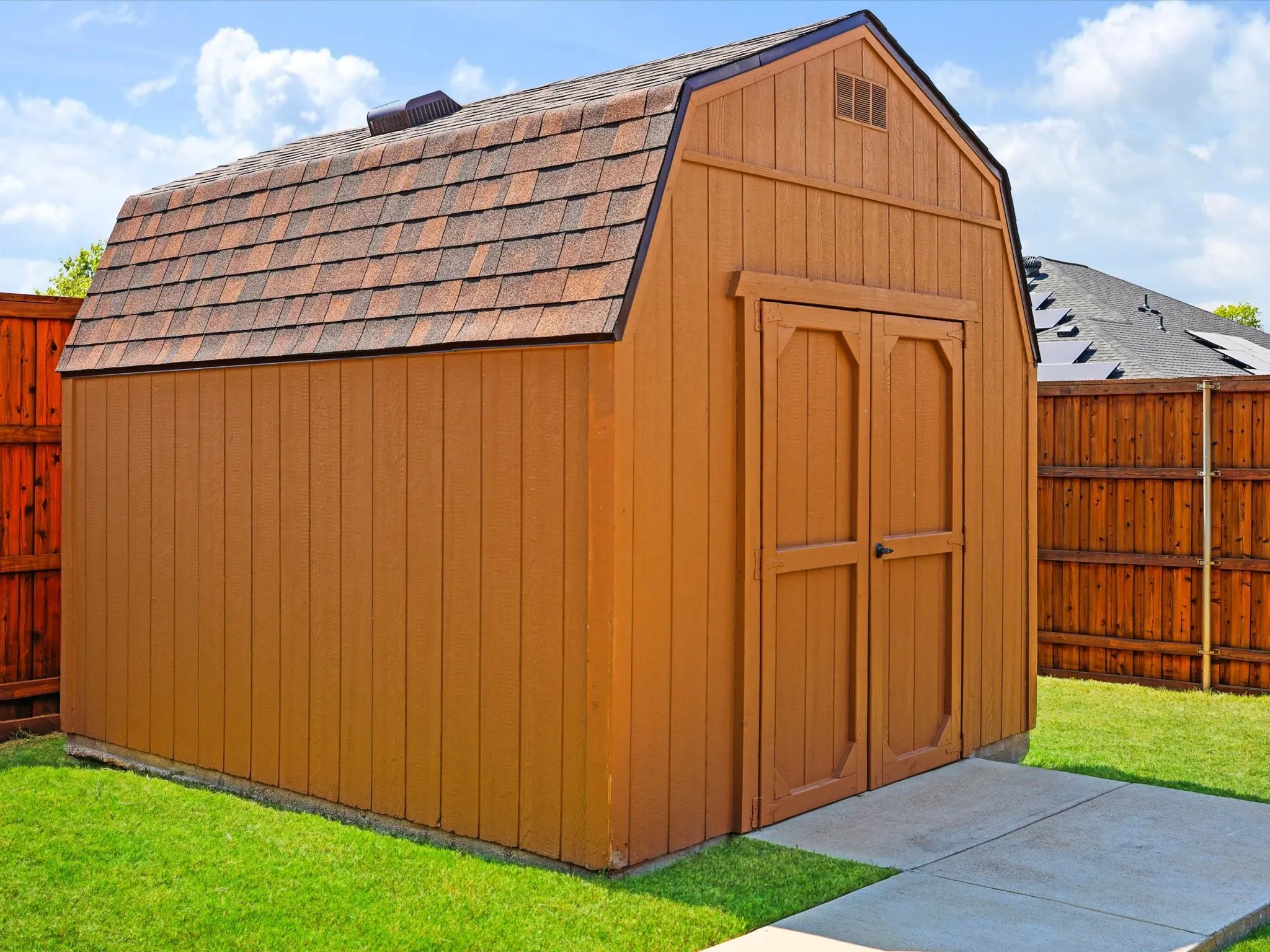 Detached storage shed with wood panel siding and an asphalt shingle roof