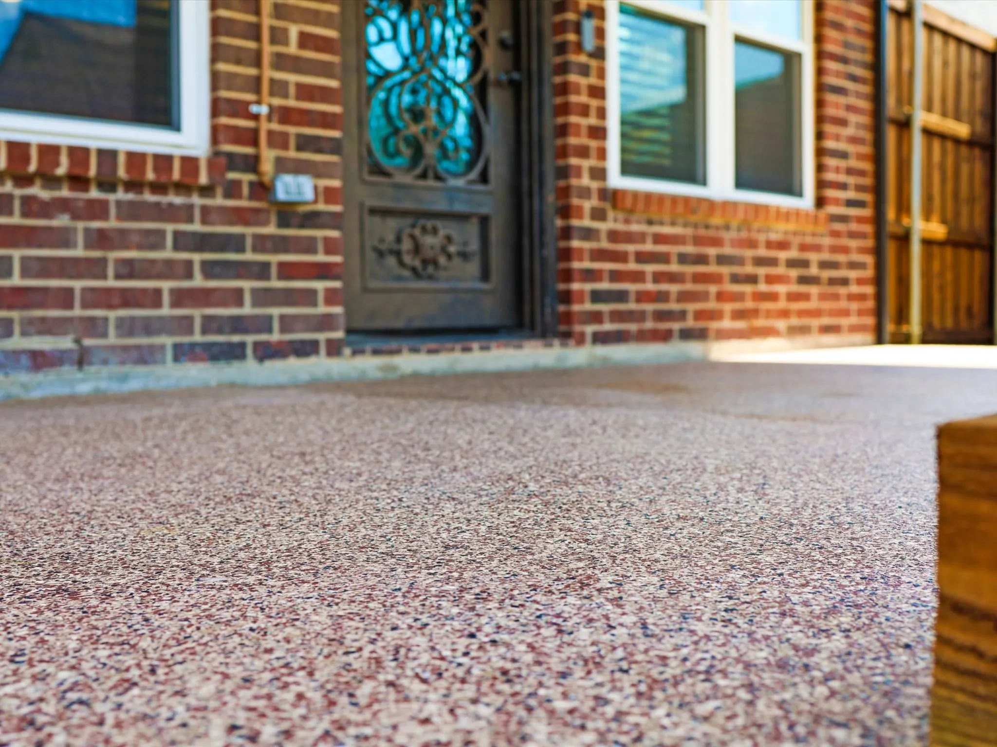 Textured composite flooring with brick exterior accents, decorative wrought iron door, and white-framed windows