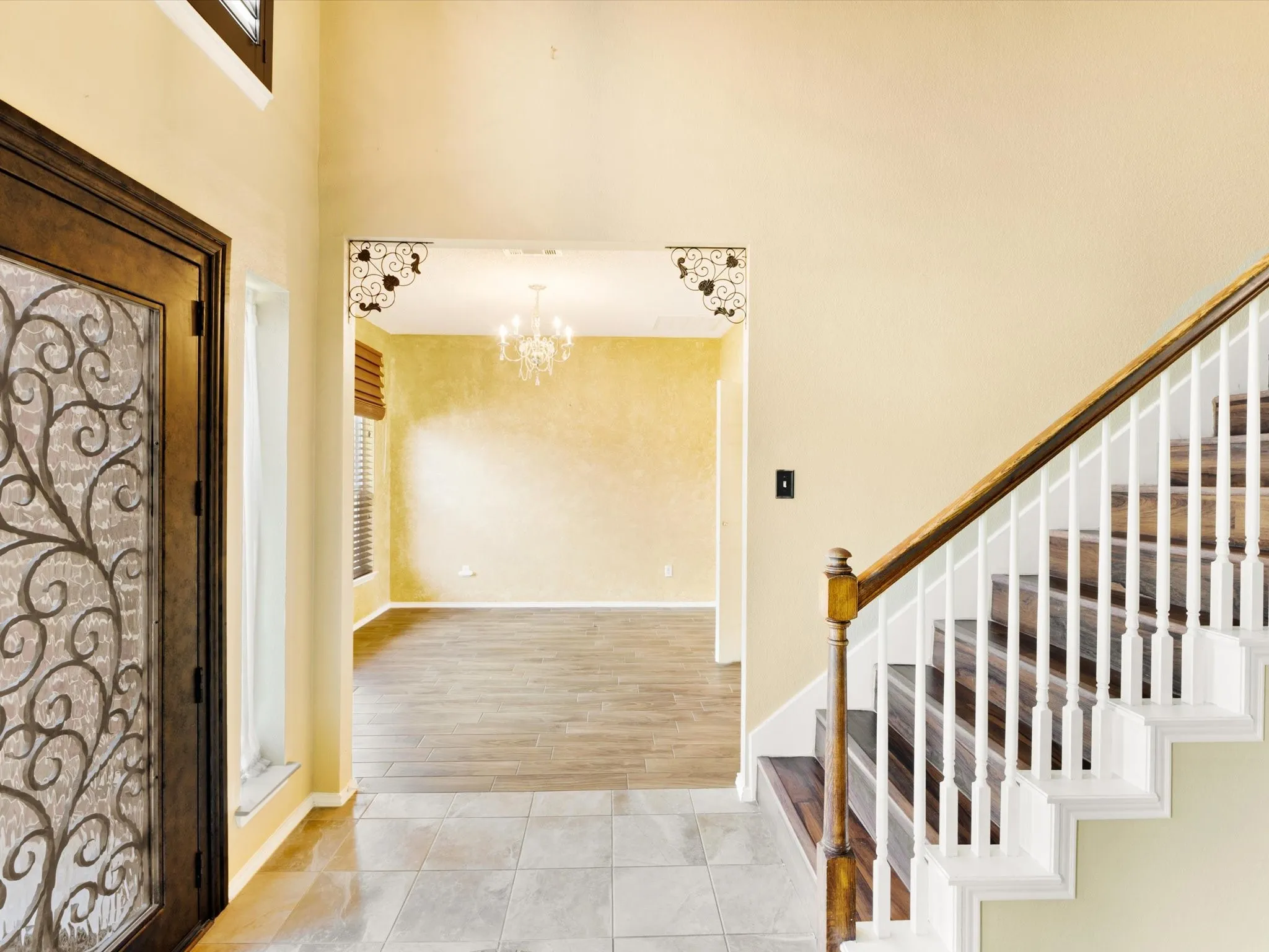 Entryway featuring tile flooring, a wood staircase with white balusters, a decorative glass front door, and an arched doorway leading to a room with wood-finish flooring and a chandelier