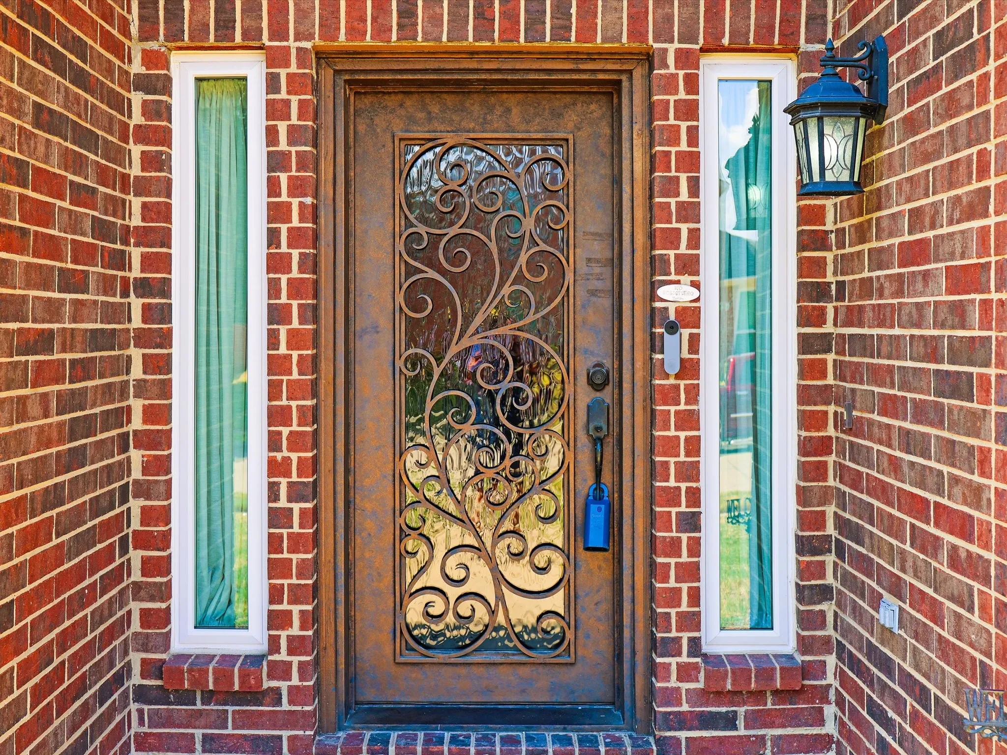 Brick facade with a decorative entry door featuring ornate wrought iron detailing and clear glass panels