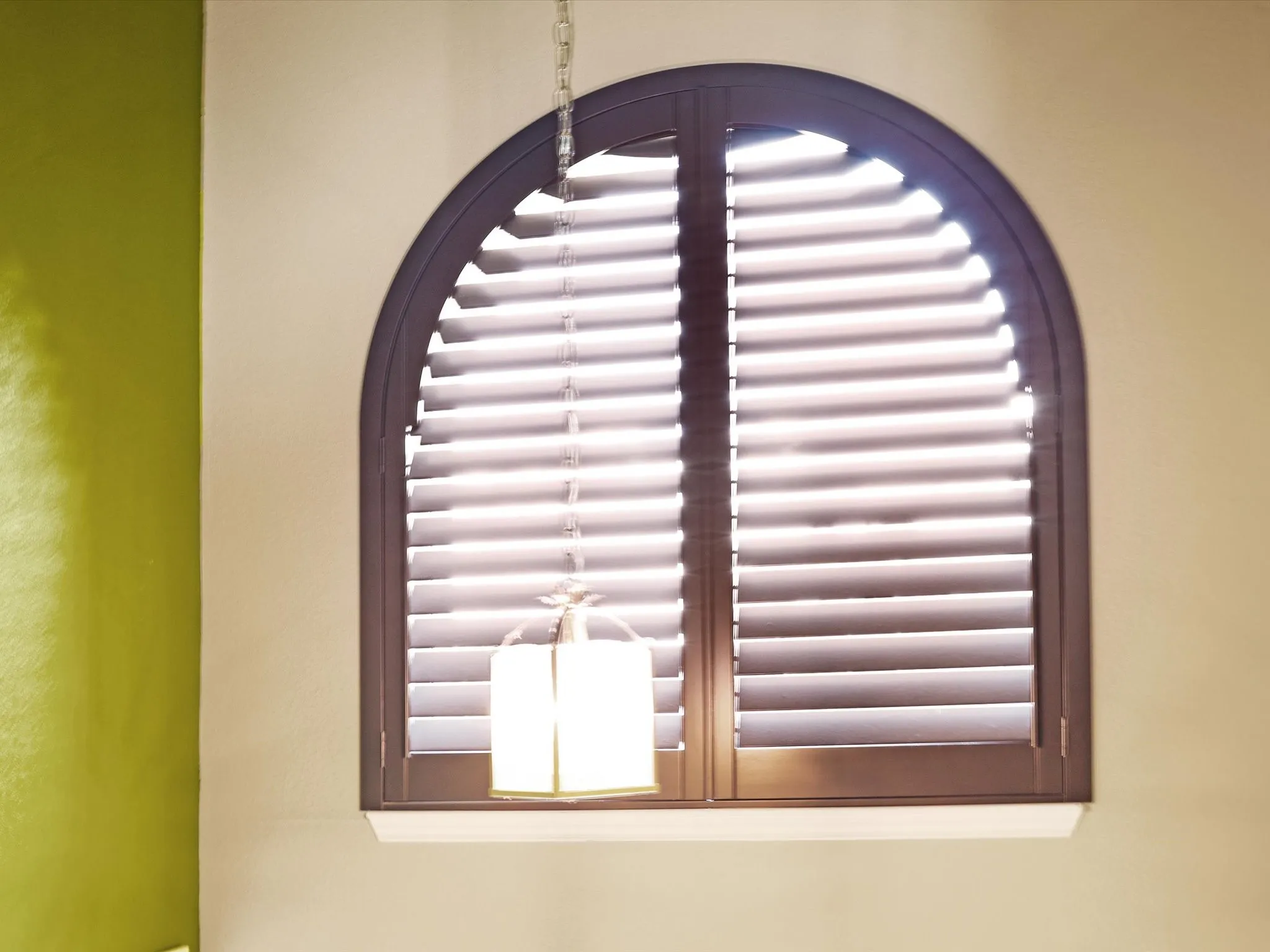 Arched window with dark wood shutters and a hanging glass pendant light fixture