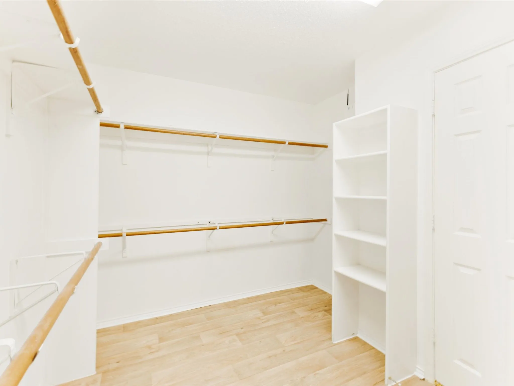 Walk-in closet featuring wood-finish flooring, white walls, multiple hanging rods, and integrated shelving units