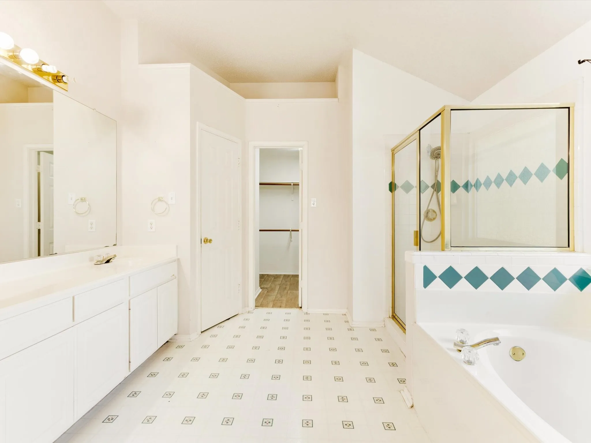 Dual vanity with integrated sinks, built-in soaking tub, glass-enclosed shower, patterned floor, and an adjacent walk-in closet