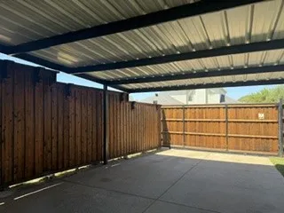 Covered outdoor space featuring a corrugated metal roof, concrete surface, and wood privacy fencing