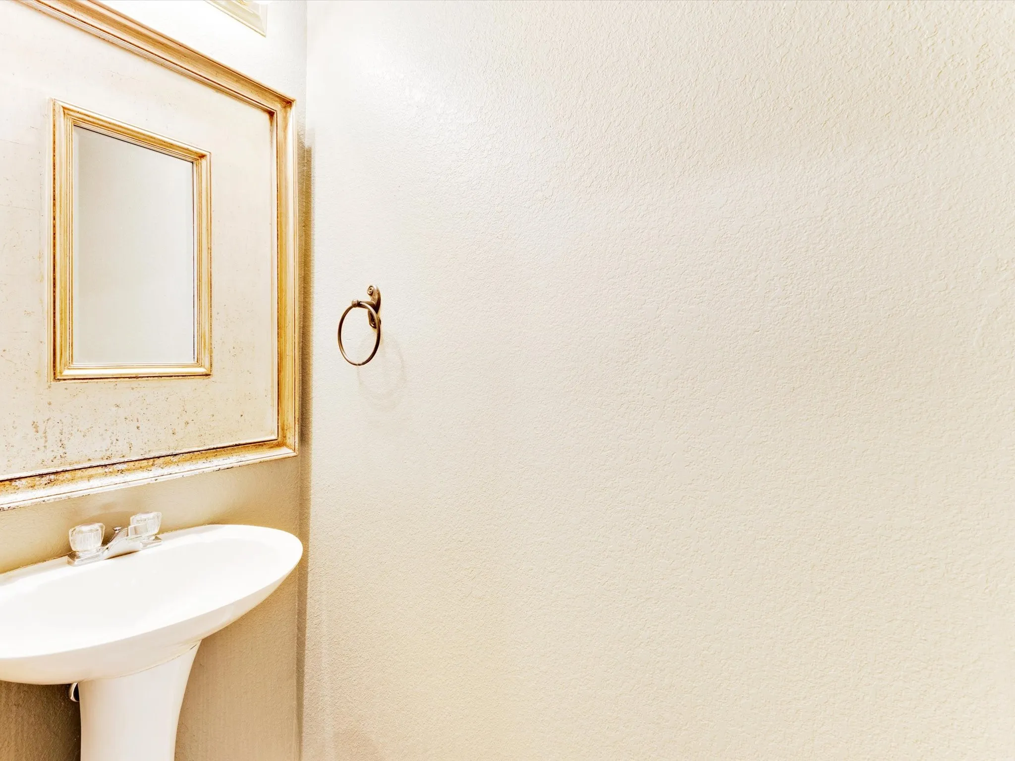 Pedestal sink with white basin, dual-handle faucet, and framed wall mirror