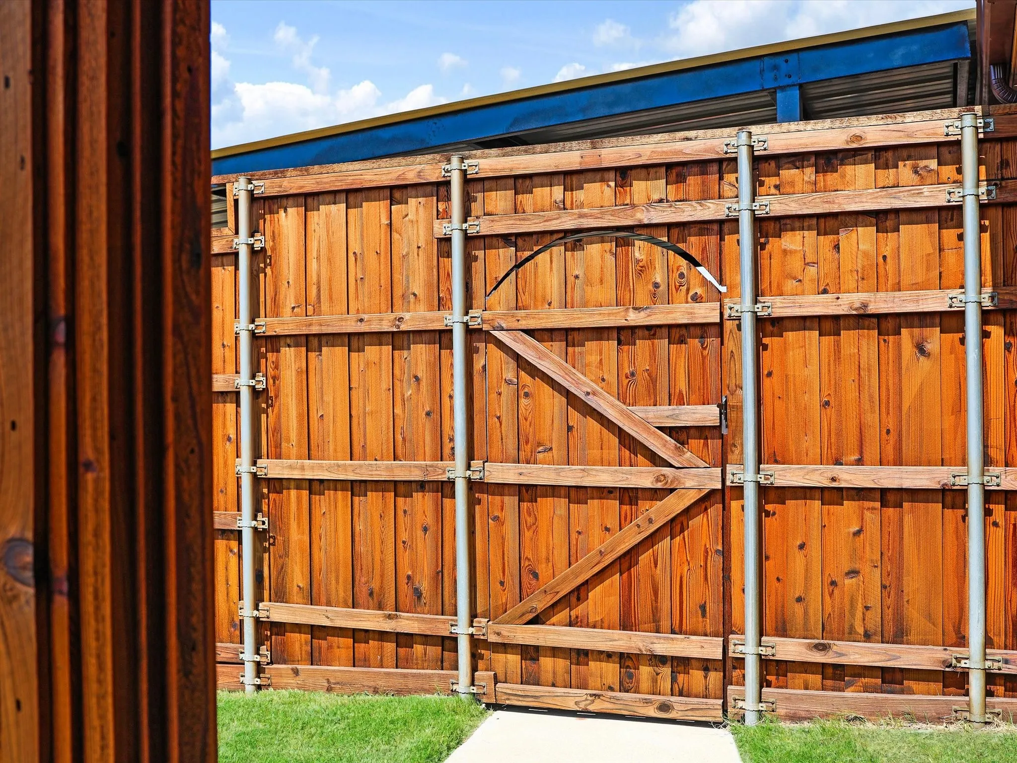 Privacy fencing featuring stained wood panels, metal support posts, and an arched gate