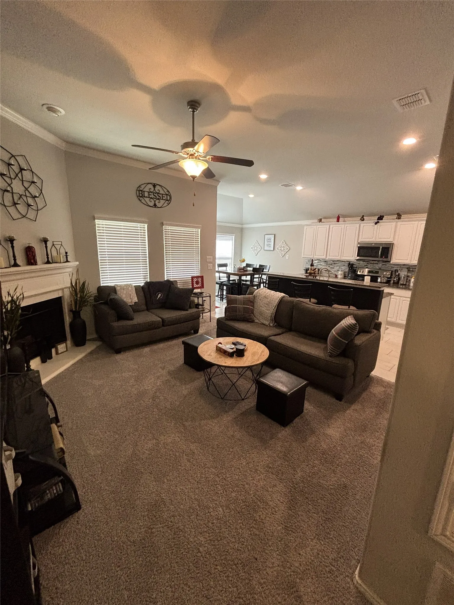 Spacious living area featuring a fireplace with a white mantel, ceiling fan, recessed lighting, and carpet flooring