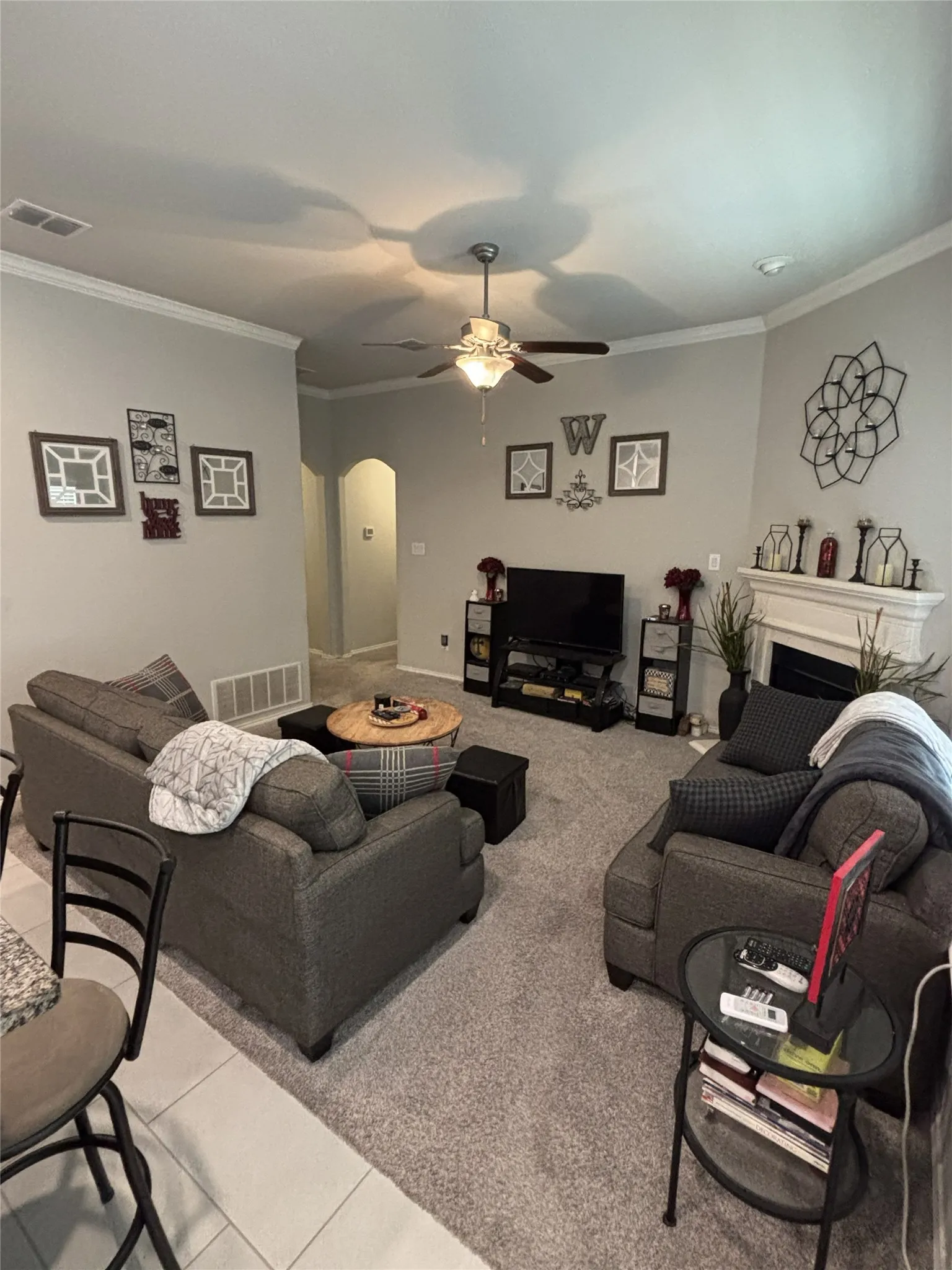 Carpeted living area with a ceiling fan, crown molding, a built-in fireplace, and an arched entryway