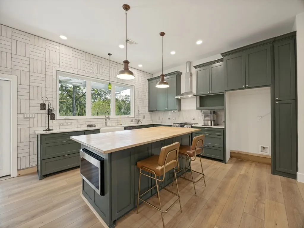 Kitchen featuring wood-finish flooring, an oversized island with an integrated microwave, a farmhouse sink, stainless steel appliances, and ample cabinetry