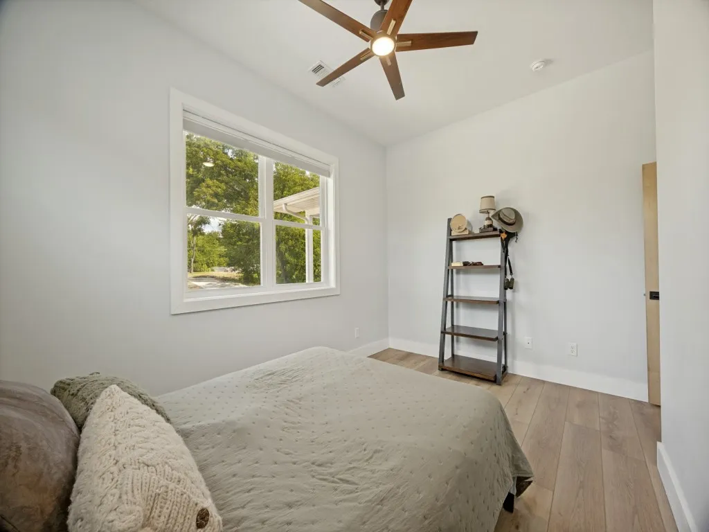 Wood-finish flooring, white walls, white window trim, and a ceiling fan with integrated lighting