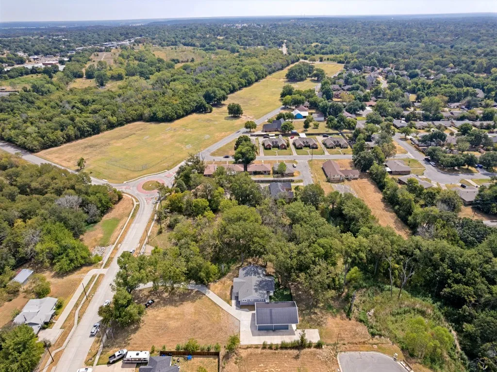 Aerial perspective featuring expansive green spaces, residential streets, a circular traffic intersection, and mature tree coverage