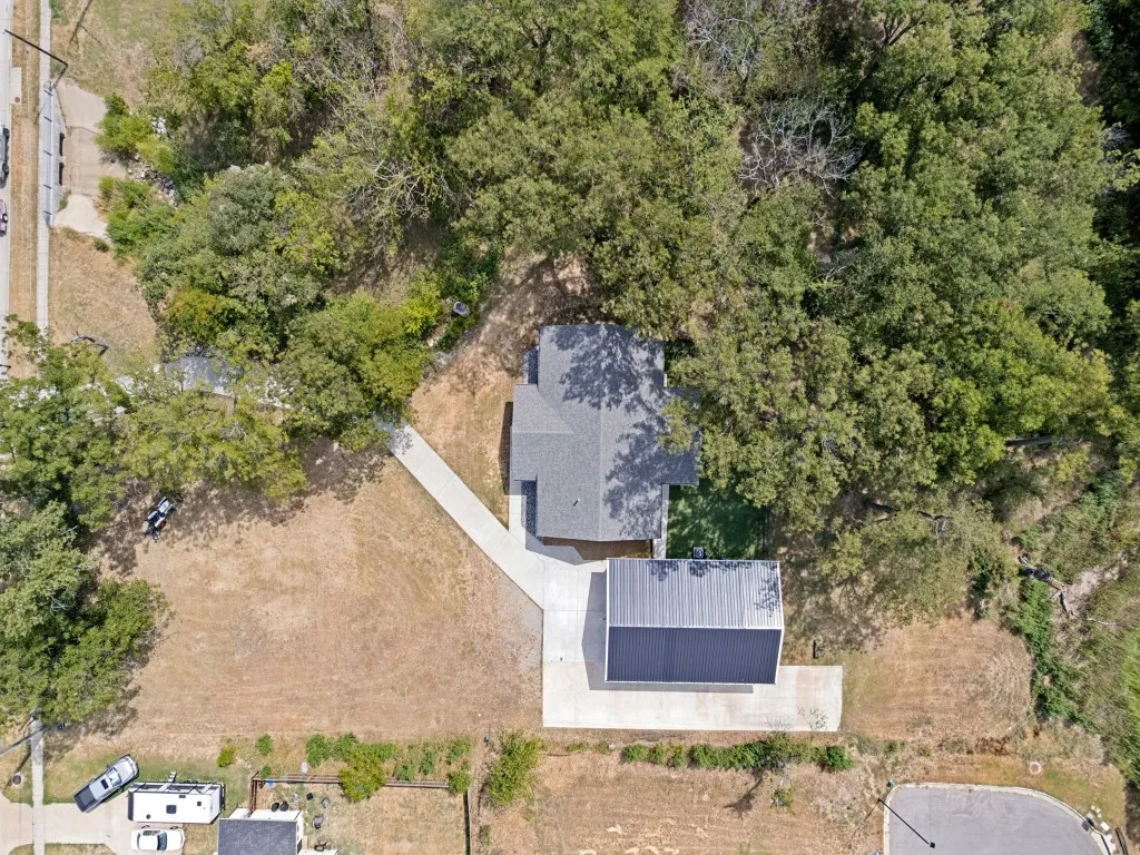 Aerial perspective showcasing a main residence with a gray shingle roof, a detached structure with a metal roof, and a concrete driveway