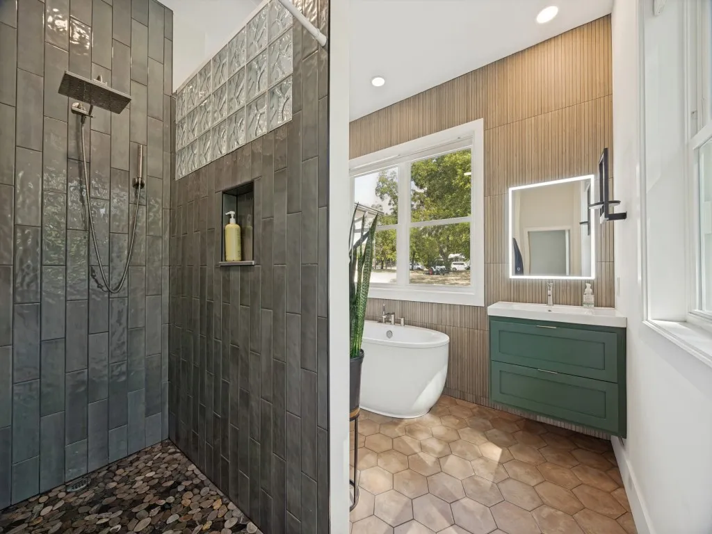 Bathroom featuring a freestanding soaking tub, a floating vanity with a vessel sink, a shower with pebble flooring, and textured wall tiling