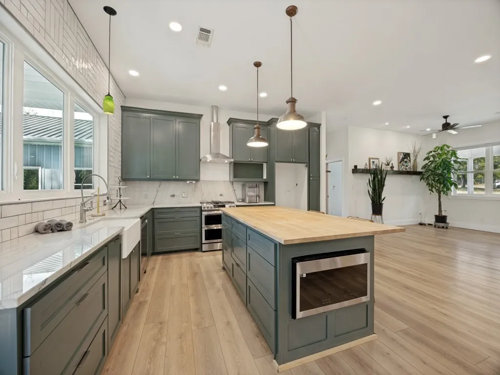 Kitchen featuring sage-toned cabinetry, light wood-finish flooring, a wood-top island with a built-in microwave, a farmhouse sink, and stainless steel appliances