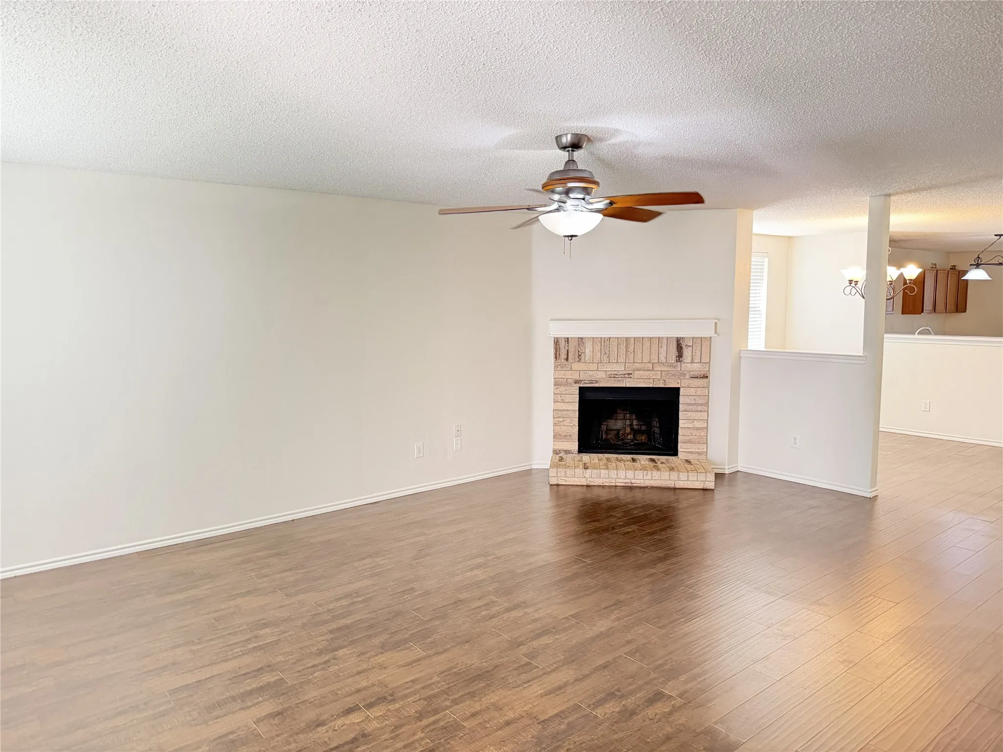 Wood-finish flooring throughout, brick fireplace with mantel, ceiling fan with integrated lighting, and a half-wall partition