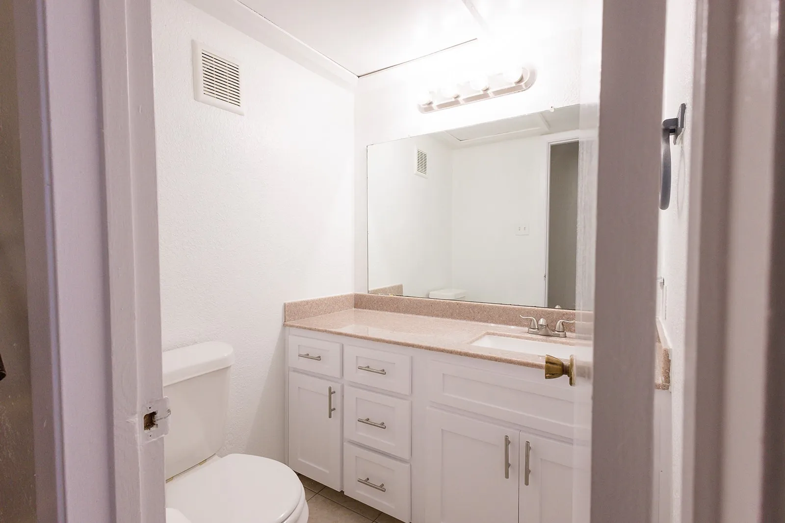 White vanity with a neutral-toned countertop, integrated sink, and wall-mounted mirror