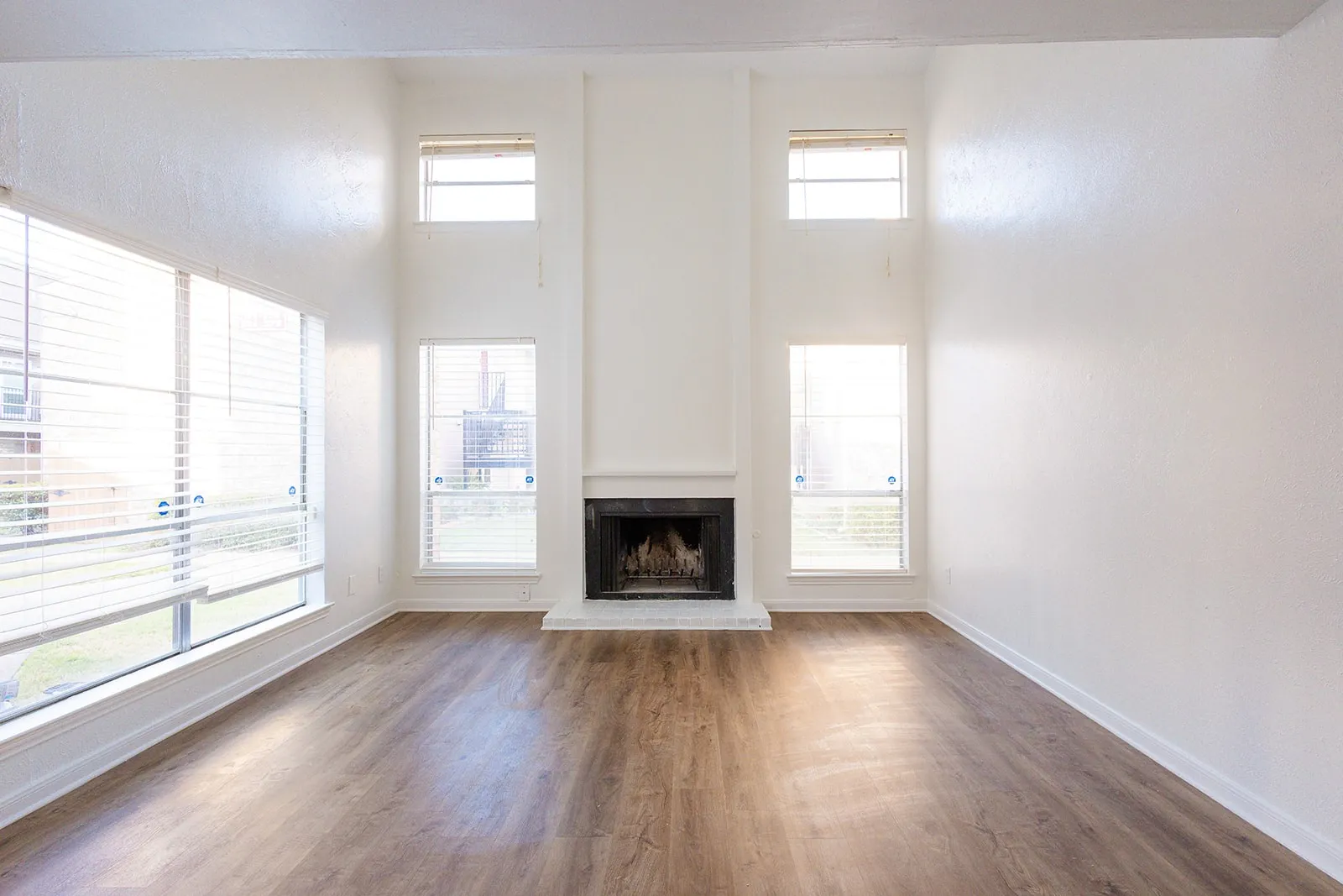 Wood-finish flooring, high ceilings, white painted walls, and a fireplace with a white mantel and hearth