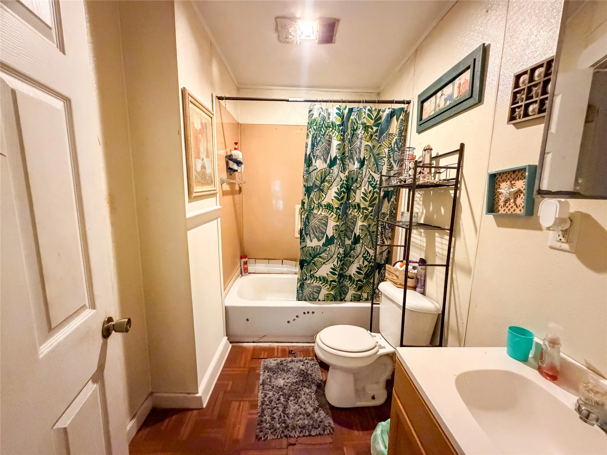 White paneled door with brass hardware, wood-finish flooring, white vanity with integrated sink, white tub, and a white toilet