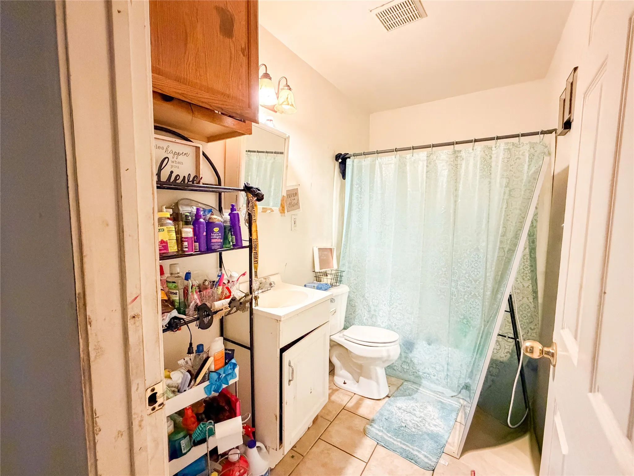 Ceramic tile flooring, vanity with integrated sink, overhead vanity lighting, built-in medicine cabinet, and a toilet