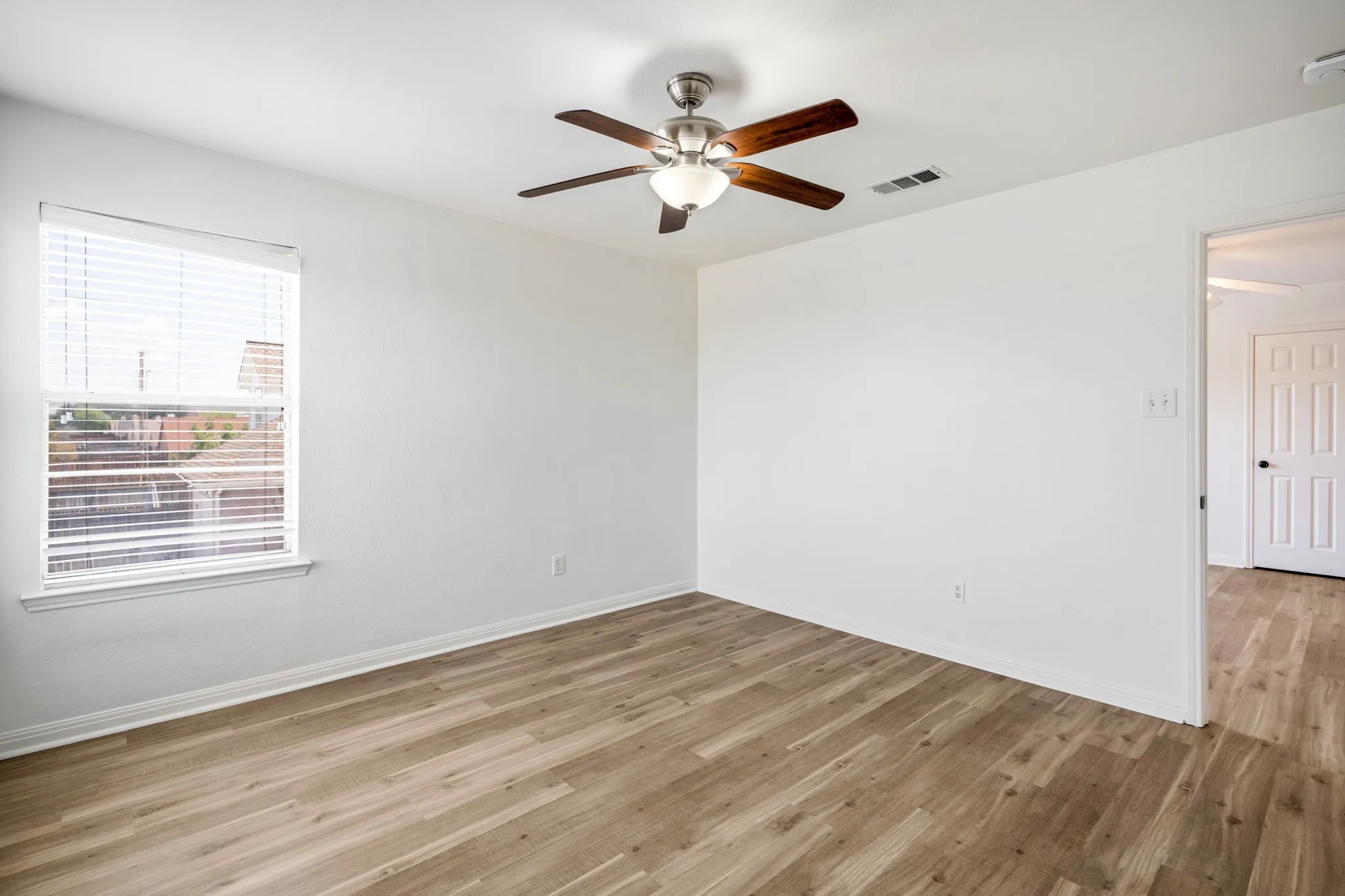 Wood-finish flooring, ceiling fan with integrated lighting, and a white paneled door