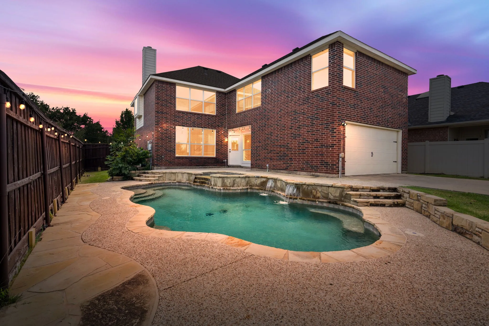 Brick exterior featuring multiple windows, a rear entry garage, and a private fence