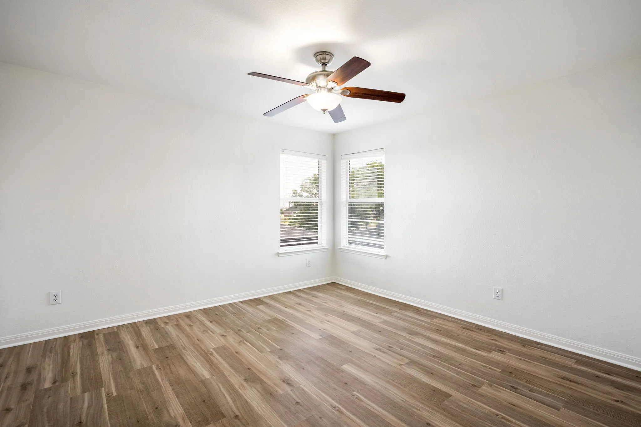 Wood-finish flooring, white walls, two windows with blinds, and a ceiling fan with integrated lighting