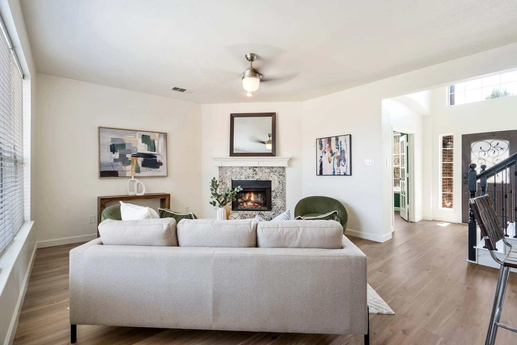 Living area featuring wood-finish flooring, a fireplace with a stone surround and white mantel, and a ceiling fan