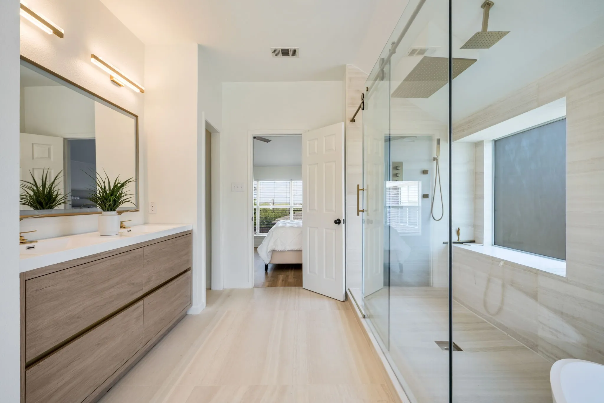 The ensuite presents natural Italian limestone on every wall and floor, a freestanding Japanese soaking tub before a picture window, a frameless glass rain shower with body jets, a floating dual vanity beneath a full width LED mirror and a Japanese smart bidet with gold fixtures throughout.