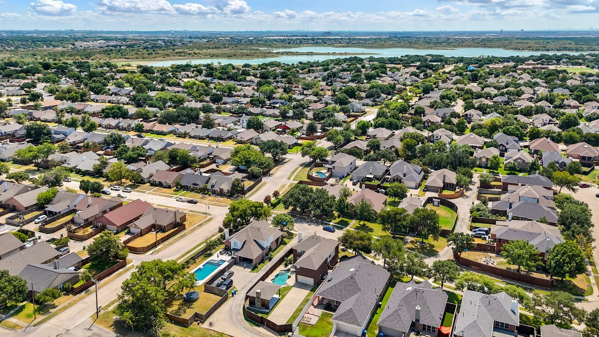 Expansive residential area featuring numerous single-family homes, mature trees, and a distant body of water