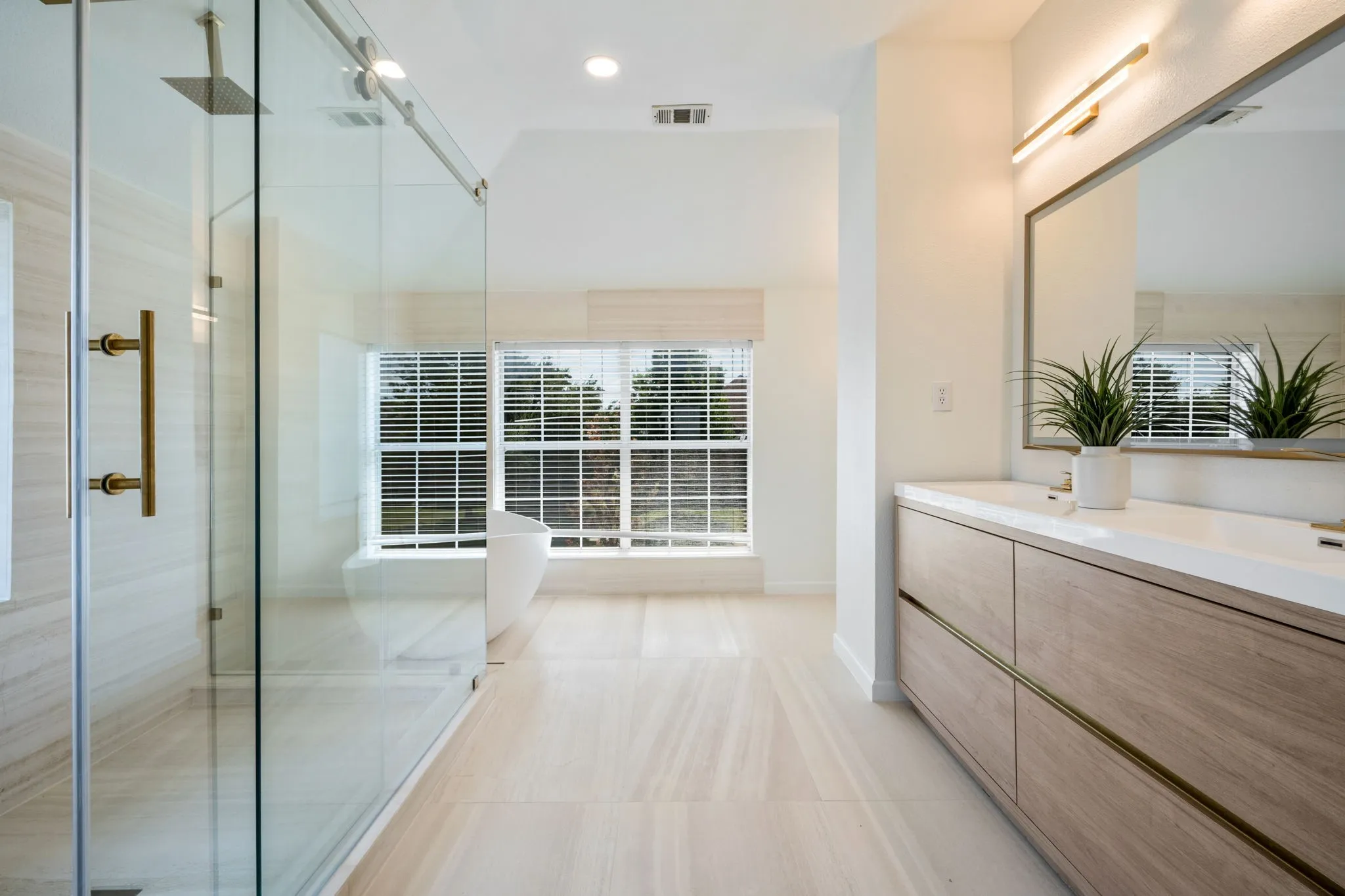 The ensuite presents natural Italian limestone on every wall and floor, a freestanding Japanese soaking tub before a picture window, a frameless glass rain shower with body jets, a floating dual vanity beneath a full width LED mirror and a Japanese smart bidet with gold fixtures throughout.