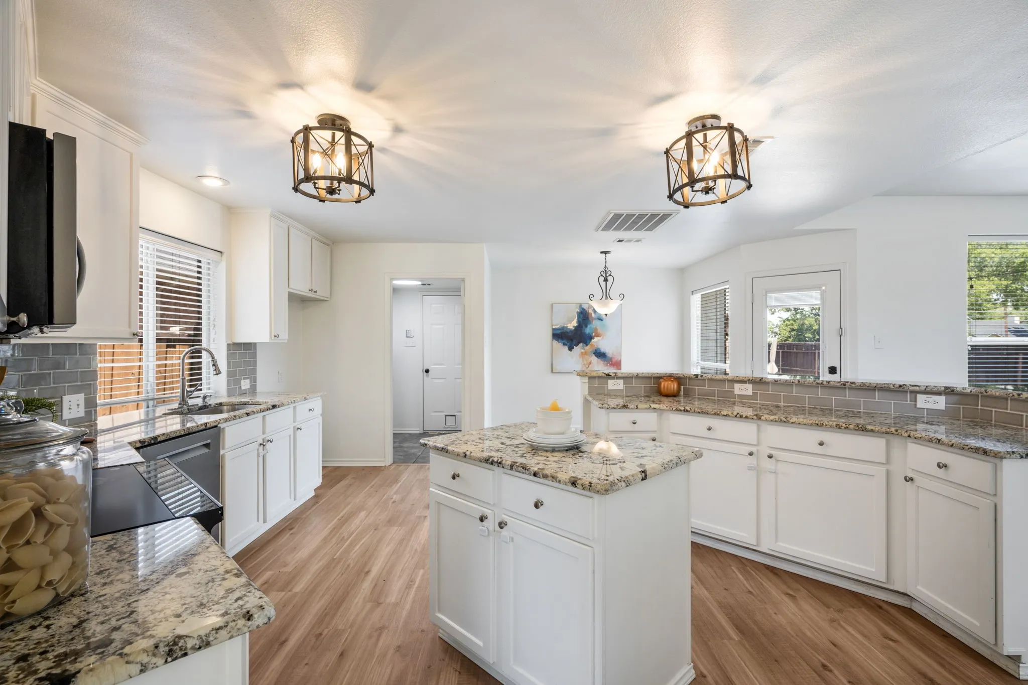 Kitchen featuring a central island, wood-finish flooring, white cabinetry, granite countertops, and a tiled backsplash